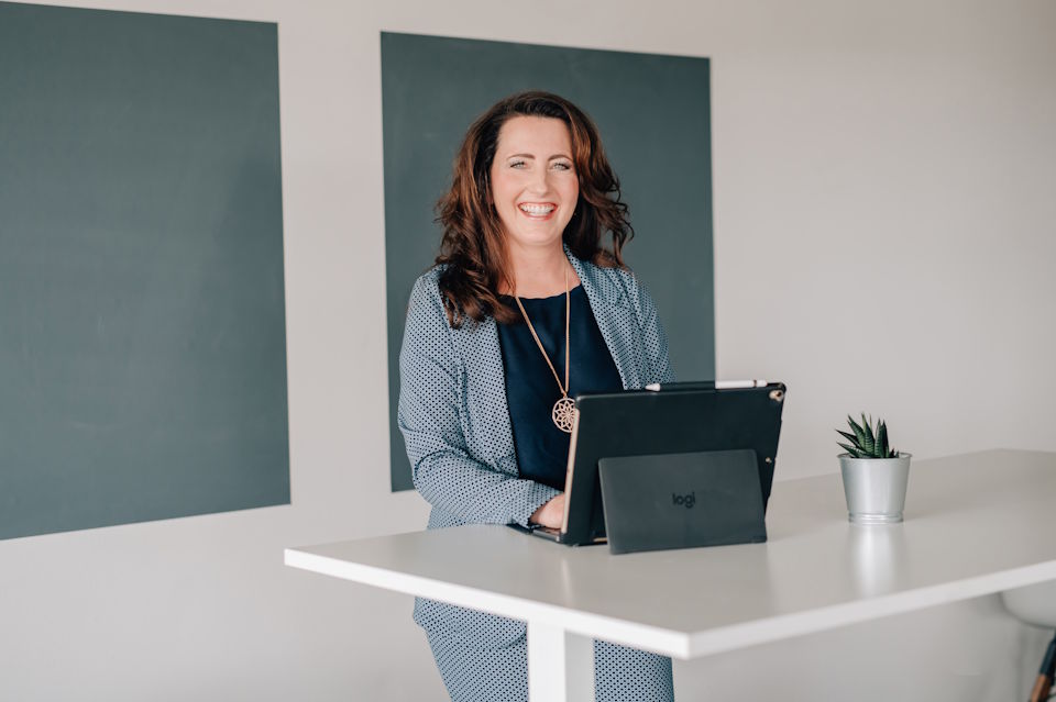 Führungskräftecoach (eine Frau) steht an einem Stehtisch mit Laptop und lächelt